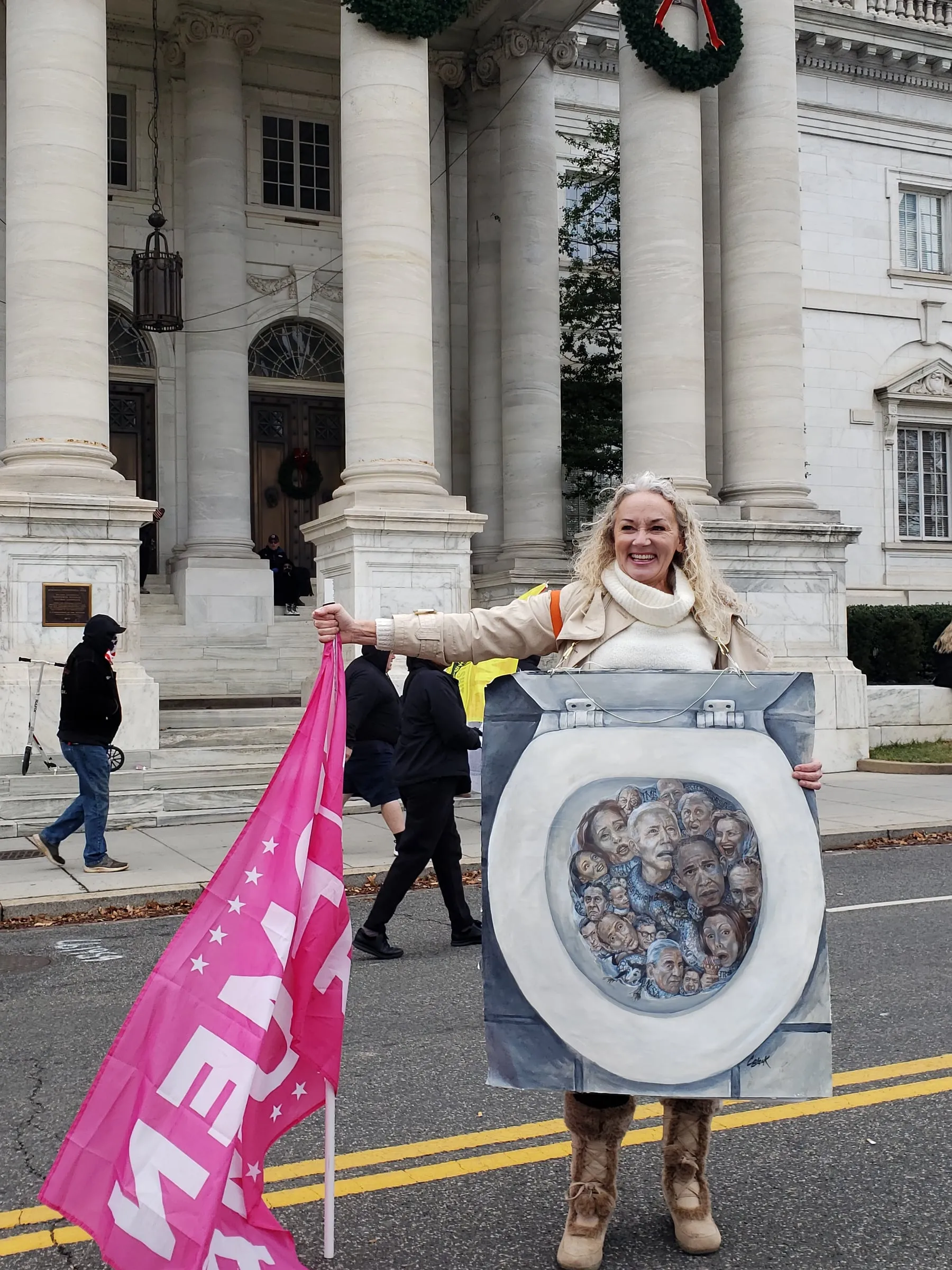 Woman holding a painted toilet seat and a pink flag in front of a columned building