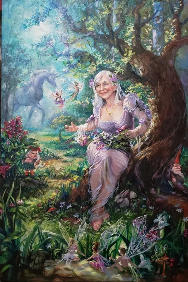 Painting by Colleen Black of a smiling woman crowned with flowers beside a large tree, with a unicorn and fairies in a meadow
